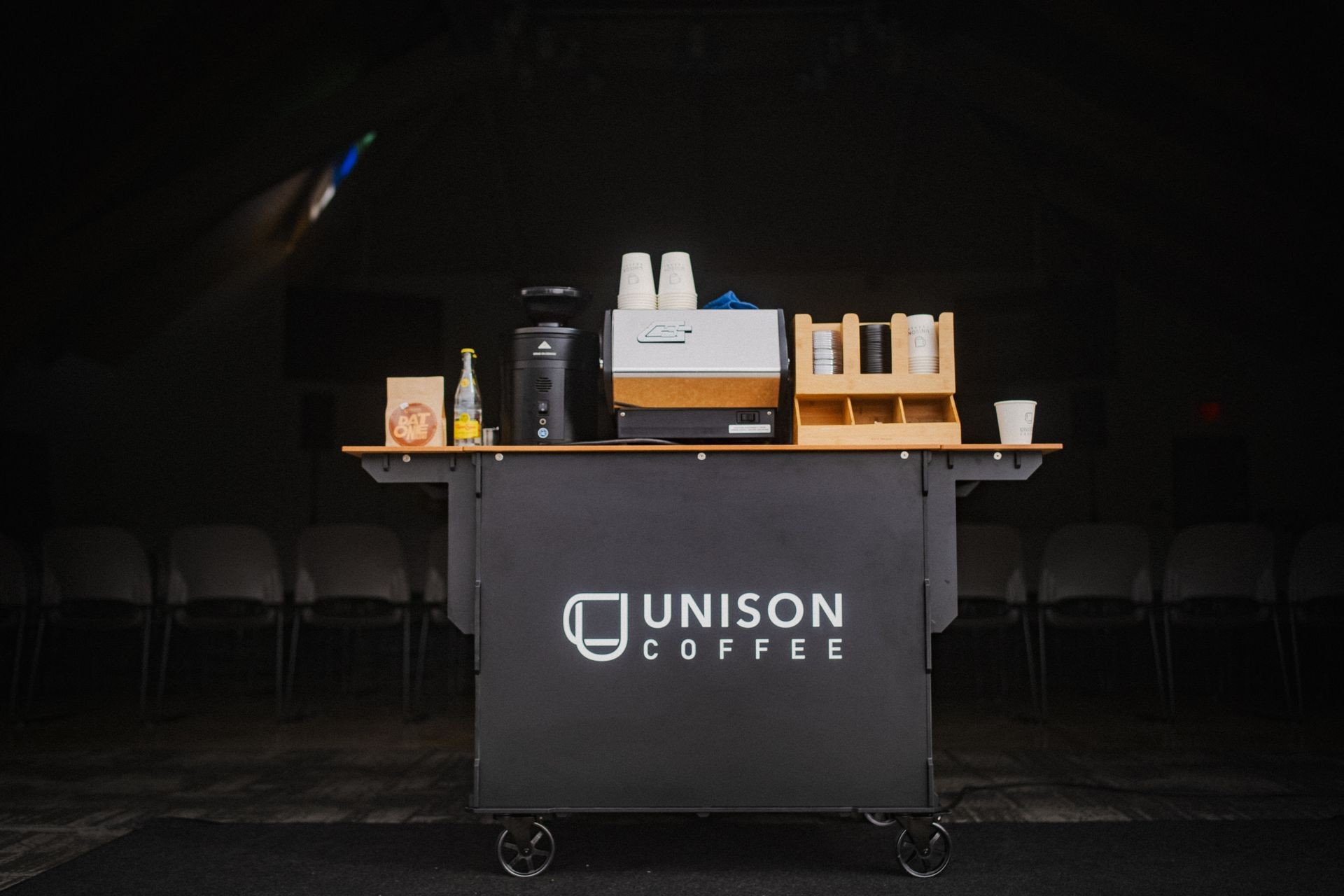 Unison Coffee cart with espresso machine, cups, and supplies in a dimly lit room.